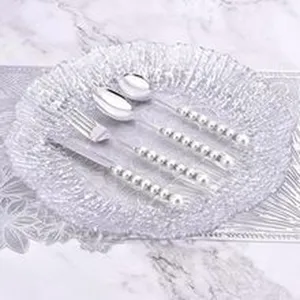 Detailansicht eines eleganten Bestecksets mit Perlengriffen auf einem Glasteller