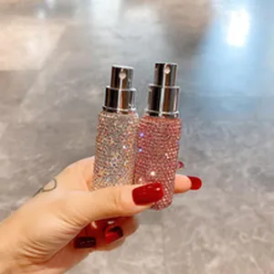 Nahaufnahme einer Hand, die zwei luxuriöse, mit Strass besetzte Sprühflaschen hält