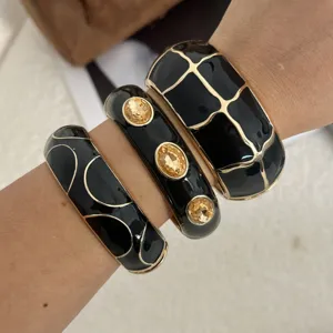 Detailansicht von drei schwarzen Emaille-Armreifen mit goldenem Gitter und gelben Kristallen.