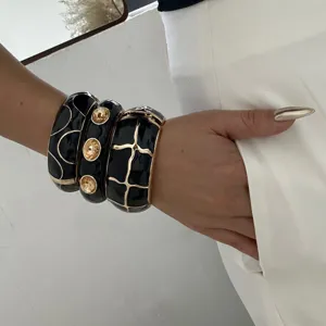 Detailansicht schwarzer Emaille-Armreifen mit goldenem Gittermuster und Kristallen