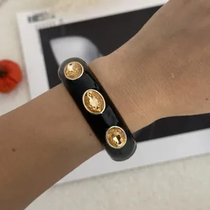 Nahaufnahme eines schwarzen Emaille-Armreifs mit drei großen bernsteinfarbenen Kristallen.