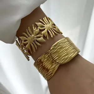 Dettaglio di bracciali a polsino dorati testurizzati con motivi a onde e fiori