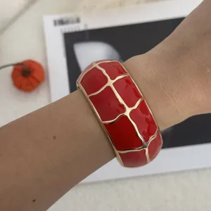 Detailaufnahme eines auffälligen roten Emaille-Armreifs mit goldenem Gittermuster.