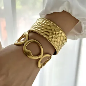 Vista dettagliata di un bracciale rigido dorato a onde e un bracciale a maglie grosse sul polso