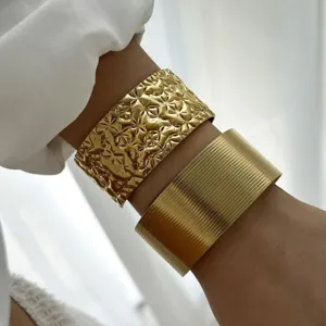 Primo piano di bracciali a polsino largo dorati e testurizzati indossati sul polso