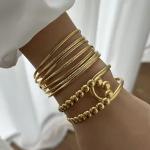 Dettaglio macro di braccialetti rigidi dorati testurizzati e polsino con perline