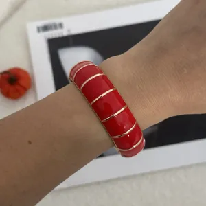 Detailansicht eines roten Emaille-Armreifs mit elegantem Goldrand am Gelenk.