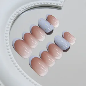 Détail macro d'ongles adhésifs dégradés bleu ciel à la française avec des pois dorés