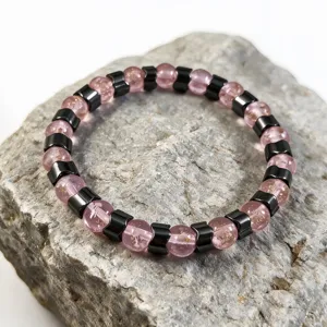 Detailaufnahme eines Armbands aus rosa Leuchtglas und Hämatit auf einem Natursteinsockel.