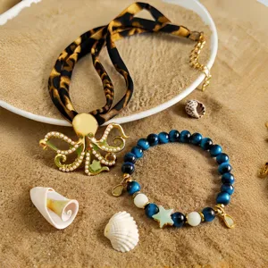 Macro view of luminous octopus necklace and star bracelet on beach sand with shells.