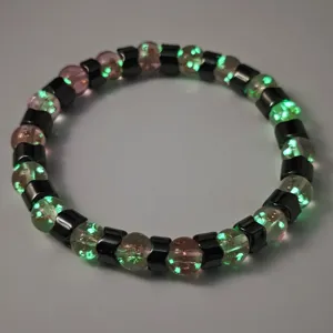 Nahaufnahme eines leuchtenden Perlenarmbands mit grün glühenden Glas- und Hämatitperlen.