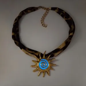 Close-up detail of a glowing blue sun pendant on a chic leopard print fabric cord necklace