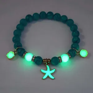 Close-up of glowing starfish charm on turquoise beaded bracelet in dark