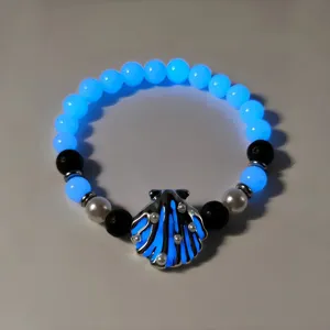 Detailed macro view of the luminous shell charm and glowing blue beads on beach necklace.