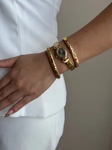 Detailed view of gold oval watch layered with red heart elastic bracelets on model's wrist.