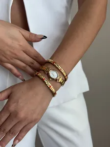 Detail showing gold oval watch stacked with red heart elastic bracelets on wrist