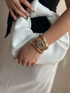 Nahaufnahme einer eleganten goldenen Quarzuhr und bunten elastischen Kristallarmbändern