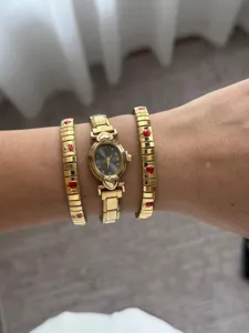 Close-up detail of gold oval watch layered with red heart elastic bracelets on wrist