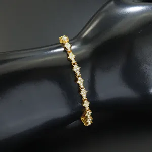 Nahaufnahme eines goldfarbenen Tennisarmbands mit floralen Kreuzen und klaren Kristallen.