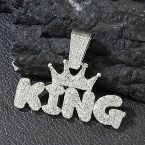 Close-up of iced out silver crown KING pendant with pavé rhinestones on dark rock.