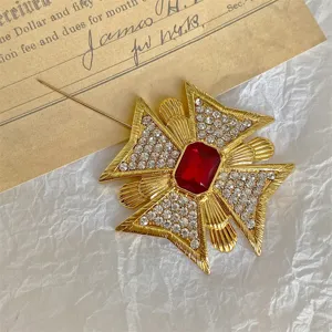 Primo piano dettagliato di una spilla a croce vintage dorata con gemma rossa e strass