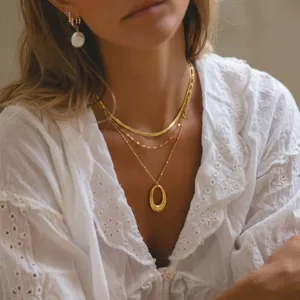 Close-up of minimalist layered gold necklace set with oval geometric pendant on model.