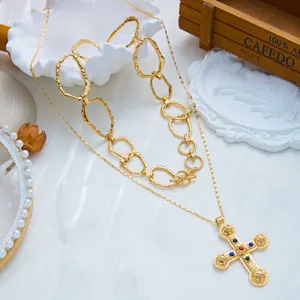 Gros plan sur une chaîne épaisse vintage dorée et collier croix avec pierres colorées.