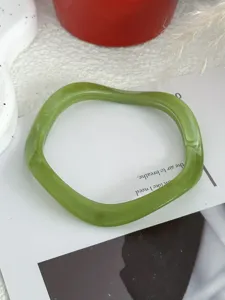 Detailopname van een stijlvolle olijfgroene golvende harsarmband met geometrisch design.