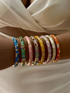 Detail showing a stack of colorful gilded floral bangles with hollow-out designs on a wrist