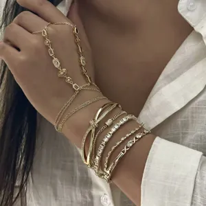 Primer plano de pulseras de oro apiladas y una cadena de mano con piedras preciosas