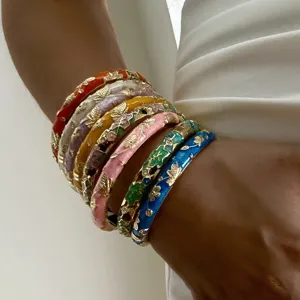 Close-up view of colorful enamel floral gold-plated bracelets worn on a model's wrist