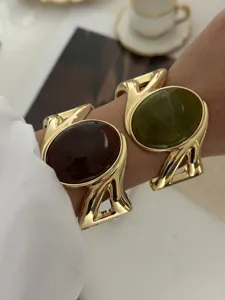 Nahaufnahme von goldenen Retro-Armreifen mit grünen und braunen ovalen Edelsteinen.