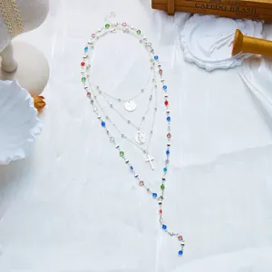 Gros plan d'un collier en Y argenté à plusieurs rangs avec croix et strass colorés.