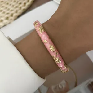 Detailed macro shot of a pink enamel bangle decorated with elegant golden leaf patterns