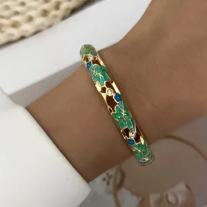 Close-up of gold-plated hollow-out floral bangle with green enamel leaves and crystals