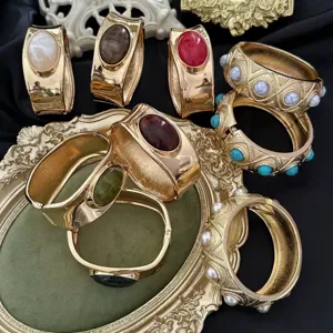 Detailansicht vintage goldfarbener Armreifen mit Edelsteinen und Perlen auf dunklem Grund