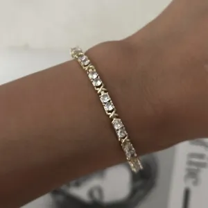 Primer plano de una delicada pulsera de tenis dorada con piedras blancas en la muñeca