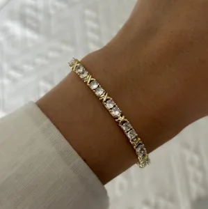 Detalle de una delicada pulsera de tenis dorada con gemas transparentes y brillantes.