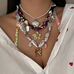 Primer plano de un collar bohemio en capas con perlas, pañuelo de seda y colgantes.