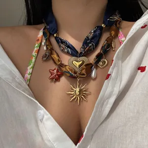 Primo piano di collana in nastro di seta con ciondoli a sole, cuore e stella marina.