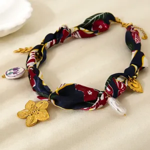 Vista de detalle de un collar de pañuelo de seda con dijes dorados y cuentas de perla.
