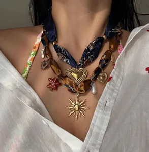 Dettaglio di una collana in nastro di seta a strati con ciondoli a cuore e sole.