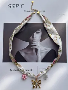 Vista detallada del collar de bufanda de seda con perlas y dijes de flores doradas.