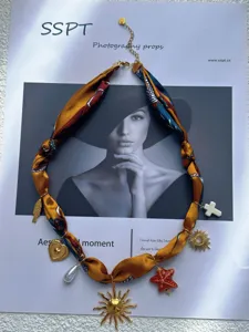 Dettaglio di una collana in nastro floreale con ciondoli dorati a sole e cuore.