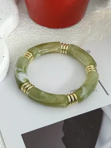 Detail van een retro groene harsarmband in bamboevorm met goudkleurige accenten.