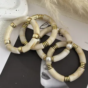 Dettaglio di bracciali in acrilico crema marmorizzato con accenti in oro e perle