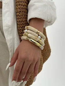 Dettaglio di bracciali in acrilico marmorizzato crema con inserti dorati indossati al polso