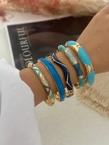 Vue détaillée de cinq bracelets joncs en émail vintage dorés portés au poignet.