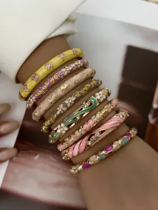 Close-up of stacked colorful pastel enamel bangles with floral patterns and crystals.