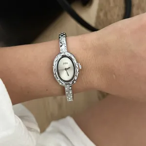 Vista ravvicinata di un orologio ovale color argento con lunetta in strass indossato al polso.